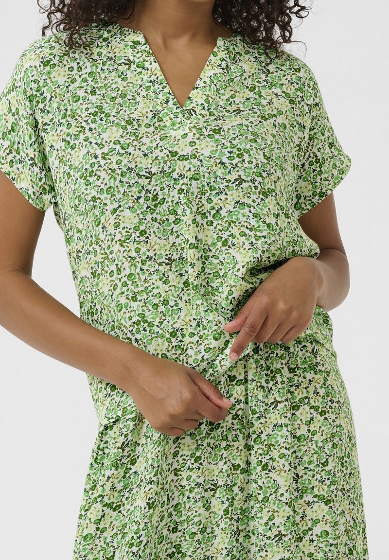 Bloemenjurk in groentinten, met een V-hals, korte mouwen en een geraffineerde taille. De stof heeft een gestructureerd, lichtgewicht uiterlijk.