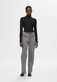 Zwarte geribde coltrui, lichtgrijze hoge taille jeans, rechte pijpen en zwarte platte schoenen. Minimalistisch ontwerp zonder zichtbare patronen of logo's.