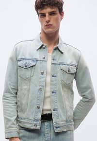 Ljusblå denimjacka med knappstängning framtill, bröstfickor och kontrasterande sömmar. Har silverfärgade detaljer och en avslappnad passform.