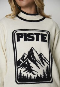 Witte trui met een zwarte geribbelde kraag, met een centrale afbeelding van bergen en bomen waarin "PISTE" in vetgedrukte zwarte letters is afgebeeld.