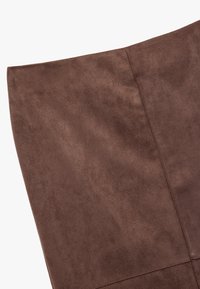Tissu en daim marron avec une texture douce, présentant une finition lisse et des détails de couture visibles le long des bords.
