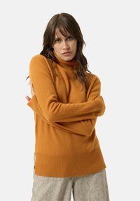 Oranžový rolák vyrobený z měkké tkaniny, zdobený žebrovanými manžetami a lemy, s volným střihem, kombinovaný se světle texturovanými kalhotami.