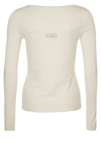 Krémový svetr s dlouhým rukávem a strukturovaným zadním dílem, který má malé dírky a logo "GUESS" z kamínků v blízkosti výstřihu.