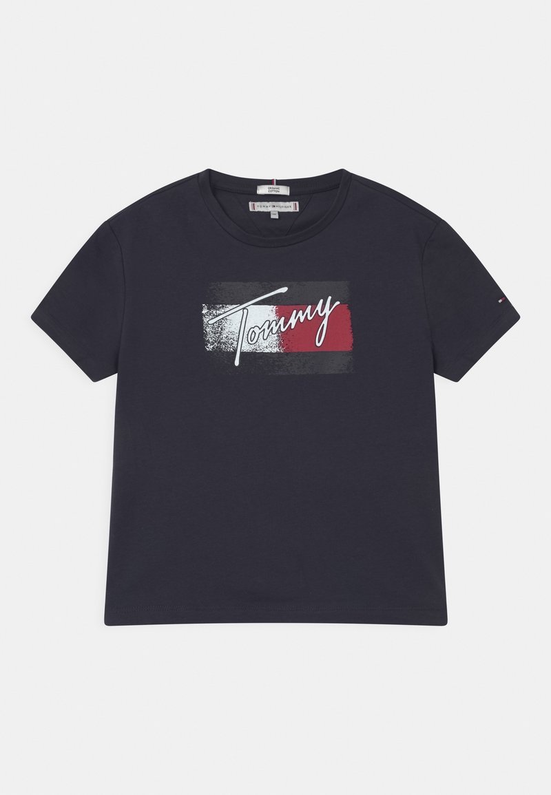 T-shirt en coton bleu marine avec un visuel central affichant le mot "Tommy" en cursive blanche, sur un bloc rouge et gris. Manches courtes.