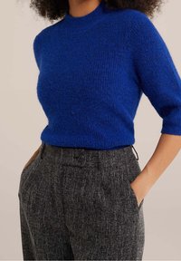 Maglione blu royal realizzato in un morbido tessuto testurizzato, con un collo alto e maniche a tre quarti, abbinato a pantaloni grigi a fantasia.