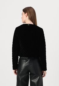 Pullover in velluto trapuntato nero con scollatura rotonda e un piccolo logo dorato sulla parte posteriore. Abbinato a pantaloni in pelle neri a vita alta.