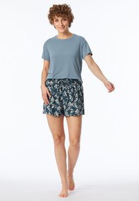 Lichtblauwe top met korte mouwen gecombineerd met donkergroene shorts met een bloemenpatroon. De shorts hebben een elastische tailleband voor extra comfort.