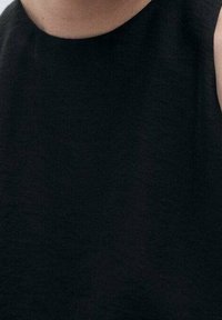 Haut noir sans manches en tissu lisse ; présente un col montant et des lignes simples et épurées sans motifs ni ornements visibles.