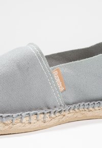 Gray canvas espadrille featuring a stitched edge, woven jute sole, and a small orange logo tag, designed for breathable casual wear.