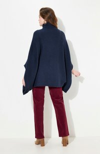 Poncho en tricot bleu marine avec un col haut, doté de manches amples et d'une coupe décontractée, associé à un pantalon en velours côtelé bordeaux et des talons blocs marron.