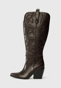 Bottes de cowboy en cuir marron avec des détails de couture, bout pointu et talon carré. Décorées de motifs ressemblant à des feuilles.