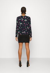 Kukallinen pitkähihaisuus pusero, jossa on peplum-vyötärö, tummansinisena ja vaaleanpunaisena, yhdistettynä tiukkaan mustaan hameeseen ja nilkkaremmiin kenkiin.