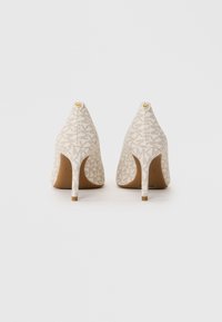 Une paire d'escarpins beiges à talons hauts avec un motif de logo MK et des détails en boutons dorés sur fond blanc, vue de l'arrière.