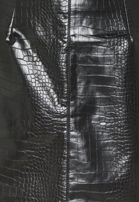 Cuir noir à motif crocodile avec une finition brillante, doté d'une fermeture éclair centrale et de bords sans coutures, mettant en avant un détail de surface texturé.