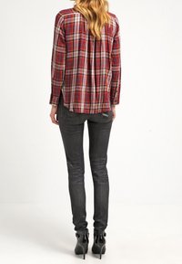 Camicia a maniche lunghe rossa e a quadri con chiusura a bottoni sul retro, abbinata a jeans neri aderenti e stivaletti con tacco.