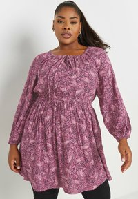 Pitkähiha tunika vaaleanpunaisena paisley-kuvioilla, jossa on joustovyötärö ja rypytetty kaula-aukko rentoa istuvuutta varten.