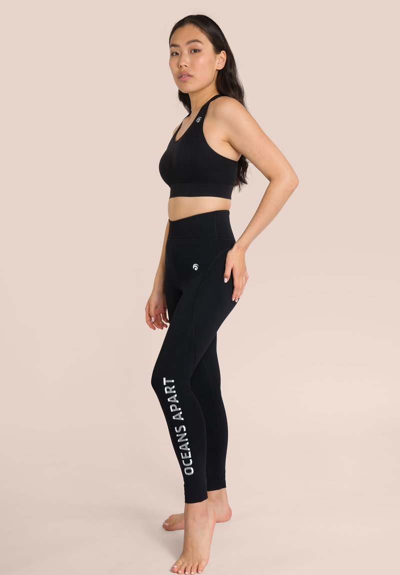 Top sportivo nero con design racerback, abbinato a leggings neri a vita alta con la scritta "OCEANS APART" in bianco sul lato.