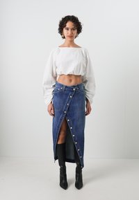 Fehér cropped ballonujjú blúz, farmerből készült csavart szoknya oldalsó gombokkal, elöl hasítékkal és térd fölé érő fekete csizmával. Egyszerű és modern dizájn.