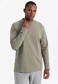 Camisa de manga larga de color caqui hecha de una tela suave. Presenta un cuello redondo y un dobladillo recto, con puños ligeramente ajustados. Diseño simple y minimalista.