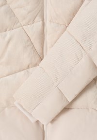 Beige jakkeærme med blandede quilterede fløjl- og glatte stofpaneler, synlig lynlås og detaljerede søm mønstre.