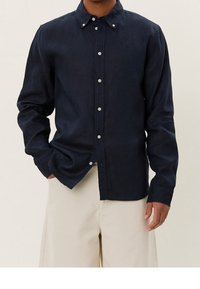 Laivastonsininen napillinen paita kevyestä kankaasta, jossa on klassinen kaulus, pitkät hihat ja hillityt napit yksityiskohdissa.