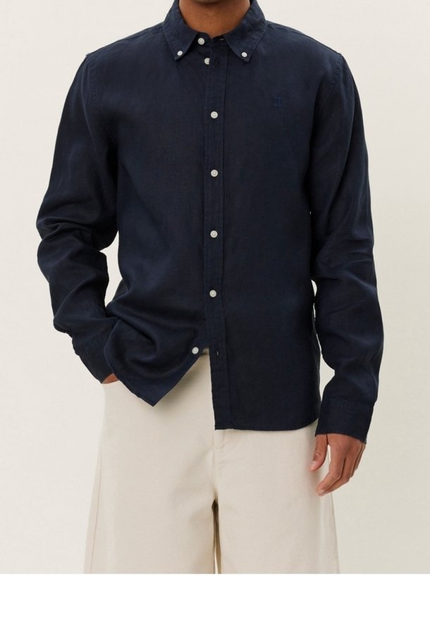 Laivastonsininen napillinen paita kevyestä kankaasta, jossa on klassinen kaulus, pitkät hihat ja hillityt napit yksityiskohdissa.