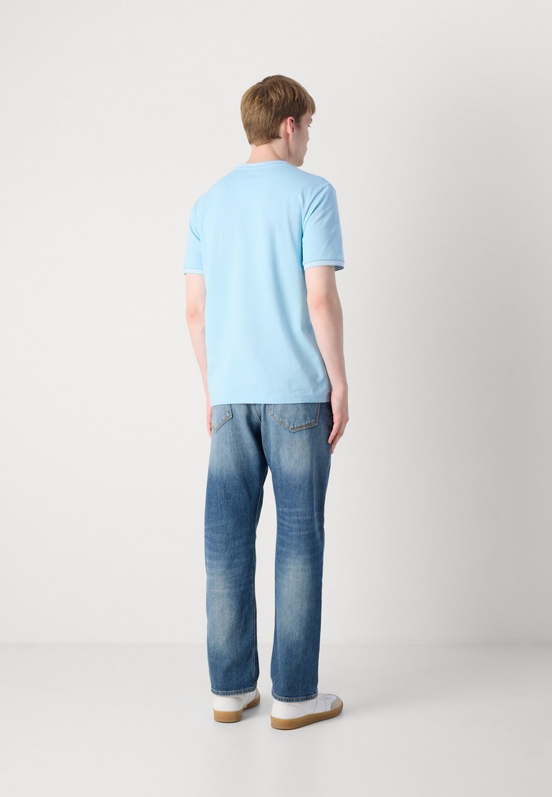 Polo shirt bleu clair à manches courtes avec un col côtelé, associé à un jean droit bleu délavé et des baskets blanches.