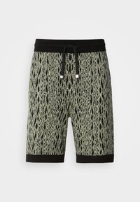 Bermudas con patrón en verde y negro con un diseño inspirado en serpientes, que cuentan con una cintura con cordón negro y un dobladillo negro contraste.