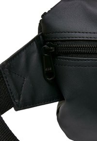 Borsa nera con superficie testurizzata, dotata di chiusura con cerniera e manico nero. I dettagli hardware includono un'evidente linguetta della cerniera e cuciture rinforzate.