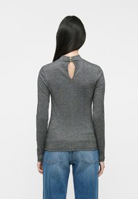 Langærmet grå top med ribbet tekstur, der har en nøglehul-rygdetalje sikret med en guldbutton, og sammen med blå denimjeans.