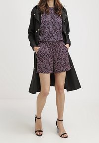 Námořnický květinový top a šortky s černým trenčkotem. Obsahuje volný střih, kapsy a černé sandály na vysokém podpatku.