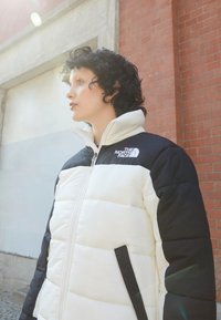 Bunda typu puffer v bielej a čiernej farbe, s vysokým golierom, zipsom, logom na hrudi a bočnými vreckami. Štruktúrovaná tkanina.