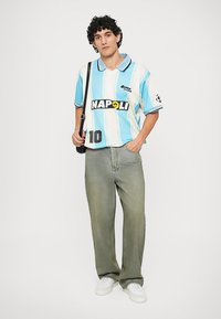 Light blue and white striped polo shirt with "NAPOLI" text, black accents, number 10, paired with faded green jeans and white sneakers.