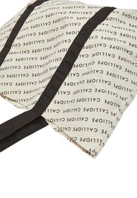 Borsa a tracolla in tela con uno sfondo crema caratterizzato da testo ripetuto in nero. Le cinghie in tessuto marrone scuro formano una forma a X nella parte superiore.