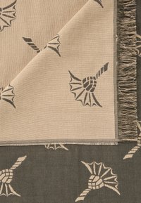 Tissu tissé avec un fond beige et des motifs de coquillage gris foncé, terminé par des bords à franges. Texture lisse, forme rectangulaire.