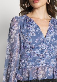 Bluse med blomsterprint i blødt, gennemsigtigt stof i blå og lilla nuancer, med V-udskæring, trækdetaljer og flagrende lange ærmer.