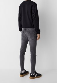 Black long-sleeve shirt, gray distressed skinny jeans, and black sneakers with white accents and a gum sole. Back view, plain background.