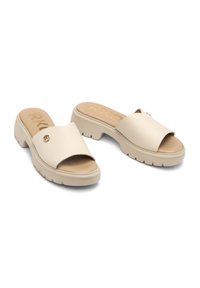 Beżowe sandały na blokowym obcasie z imitacji skóry, z szerokim, gładkim paskiem i teksturowanym wykończeniem. Zawierają złoty akcent i wyściółkę na wkładce.