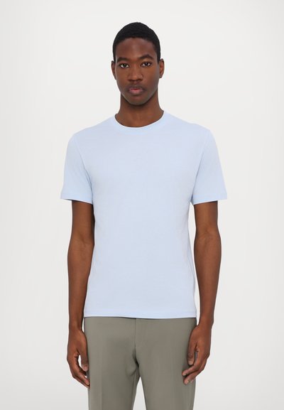 Tricou bleu deschis cu guler rotund, fabricat din material moale, design ajustat cu mâneci scurte, textură netedă, purtat cu pantaloni de culoare deschisă.