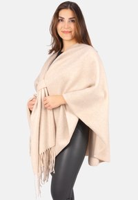 Beige Poncho aus weichem Stoff, mit einem Wickeldesign, das in der Mitte gebunden ist und mit Fransen am Saum verziert ist. Glatte Textur mit lockeren Ärmeln.