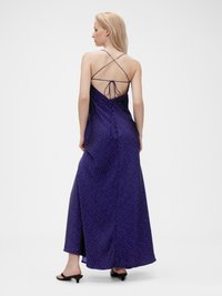 Langes Maxikleid aus lila Satin mit weißen Punkten, mit tiefem Rückenausschnitt, gekreuzten Trägern und fließender Passform. Geschmeidige Textur und elegante Silhouette.