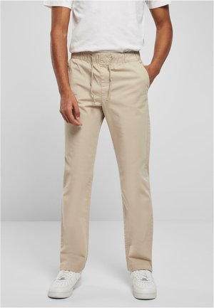 Beige, lette bukser med elastisk talje, snøre og sidelommer, parret med hvide sneakers. Glat stoftekstur.