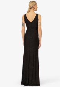 Schwarzes, ärmelloses Kleid mit V-Ausschnitt, das bodenlang ist, eine glatte Textur aufweist und dezente funkelnde Akzente überall hat.