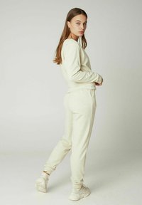 Ensemble de sweatshirt et de joggers en coton beige. Le sweatshirt a des manches longues et une taille ajustée, tandis que les joggers ont une coupe décontractée et des chevilles resserrées.
