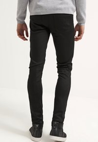 Jeans noirs avec une coupe slim et de subtils détails de couture, associés à des baskets grises montantes à la cheville avec des zippers pour un enfilage facile.