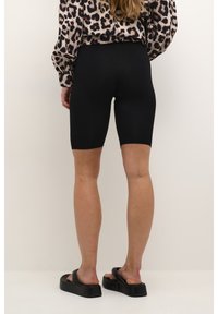 Shorts de ciclismo negros de cintura alta, hechos de un tejido elástico, con un diseño ajustado. Combinados con una blusa estampada y sandalias negras tipo slides.