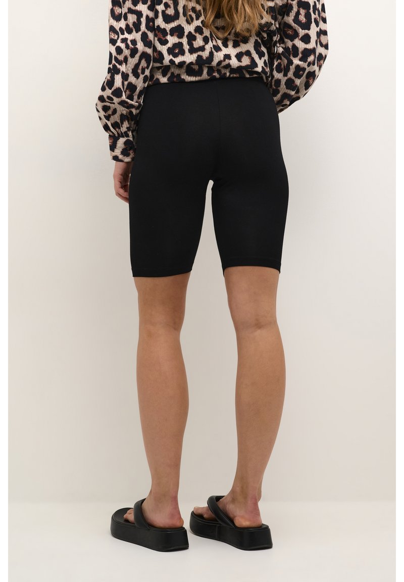 Shorts de ciclismo negros de cintura alta, hechos de un tejido elástico, con un diseño ajustado. Combinados con una blusa estampada y sandalias negras tipo slides.