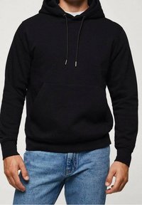 Sweat à capuche noir en tissu doux, avec poche kangourou, capuche à cordon et poignets et ourlet côtelés. Porté avec un jean bleu.