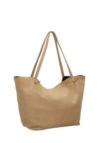 Bolso tote de ante beige con dos correas largas, que presenta una textura suave y un diseño de abertura superior. El interior parece negro. No tiene herrajes ni acentos visibles.