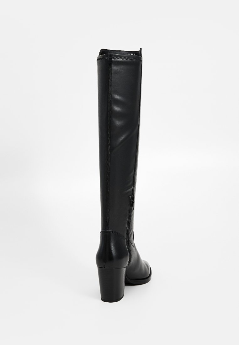 Botte en cuir noir haute avec un talon carré et une fermeture éclair sur le côté, vue de l'arrière sur fond blanc uni.